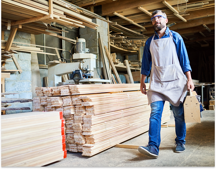 a worker with safety equipment walking past a pile of lumber